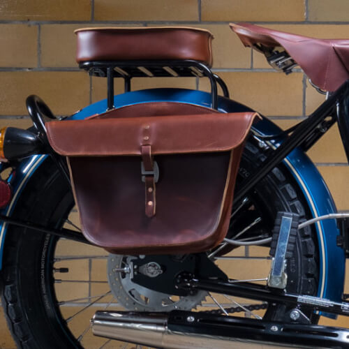 Brown leather motorcycle saddlebag on a blue bike against a brick wall.