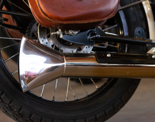 Close-up of a motorcycle exhaust pipe and wheel with leather seat.