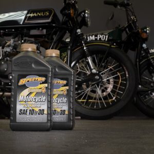 Two bottles of Spectro motorcycle oil in front of vintage motorcycles in a garage setting.