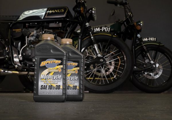 Two bottles of Spectro motorcycle oil in front of vintage motorcycles in a garage setting.