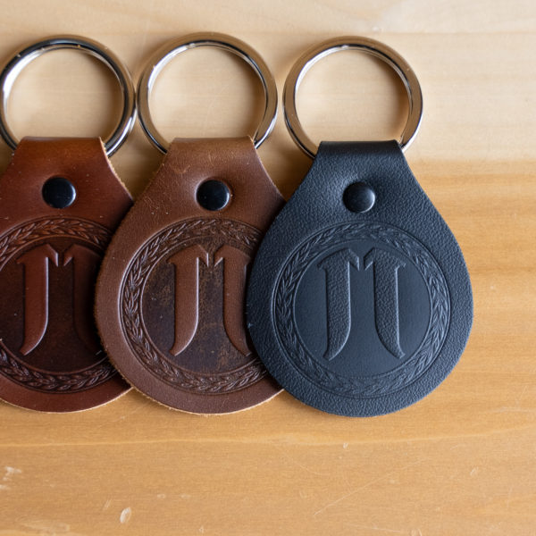 Three custom leather keychains with monogram initials on a wooden surface.