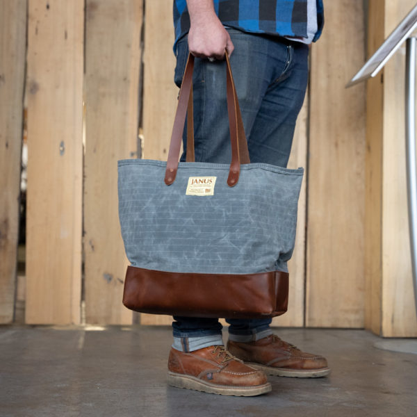 Person holding a stylish gray and brown tote bag with a JANUS label.