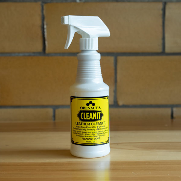 Spray bottle of Obenauf's Leather Cleaner on wooden surface with brick background.