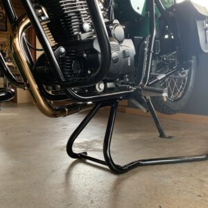 Close-up of a motorcycle's engine and chromed exhaust on a center stand in a garage.