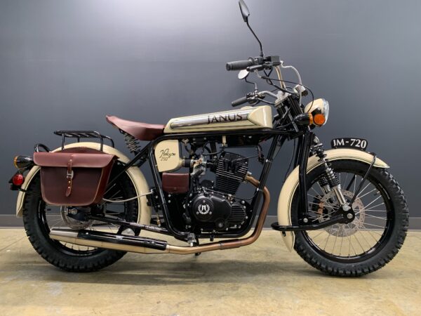 Vintage Janus motorcycle with cream body and brown leather saddlebags against a grey wall.