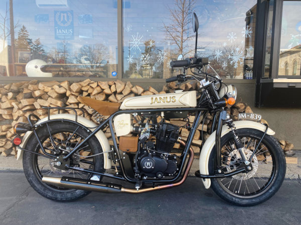 Vintage Janus motorcycle parked outside with a woodpile and snowflake decorations.