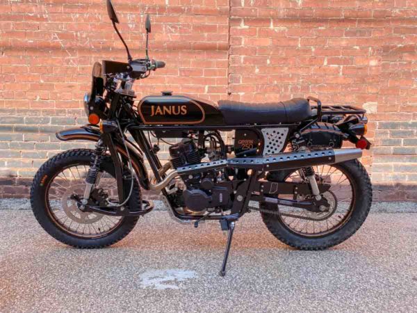 Vintage-style black Janus motorcycle parked against a brick wall.