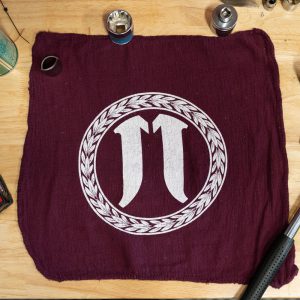 Burgundy cloth with white Pi symbol and circular wheat motif on a wooden table with bike parts.