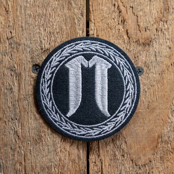 Embroidered monogram coaster with initials on wooden background.