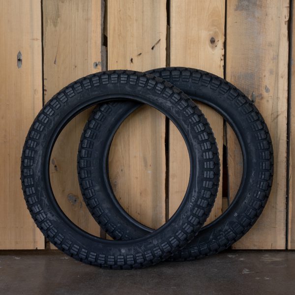 Two new motorcycle tires leaning against a wooden wall.