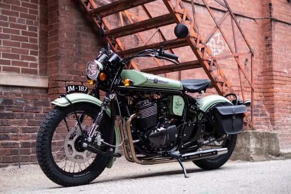 Green vintage motorcycle parked on urban brick street.