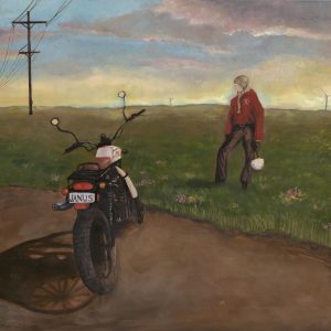 Person standing next to a motorcycle in a field at dusk, power lines and wind turbines in the background.