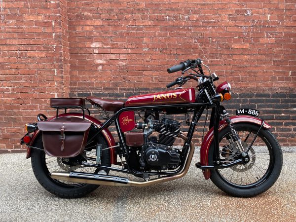 Classic Janus motorcycle parked against a brick wall.