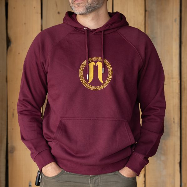 Person in maroon hoodie with golden emblem design standing against wooden background.