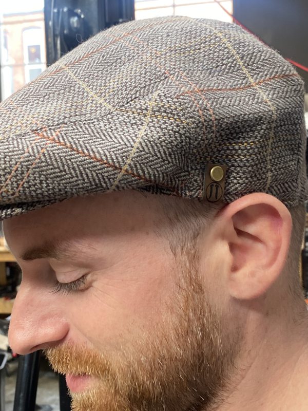 Close-up of a man wearing a tweed flat cap with button detail.