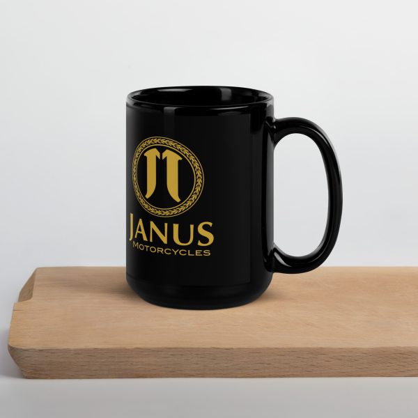 Black coffee mug with Janus Motorcycles logo on wooden surface.