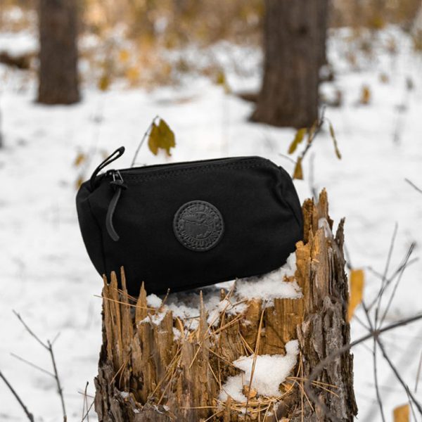 Black zipper pouch on a snowy tree stump in a forest.