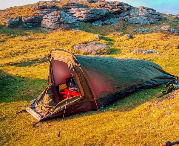 Camping tent pitched on grassy hillside during sunset, adventure outdoor concept.