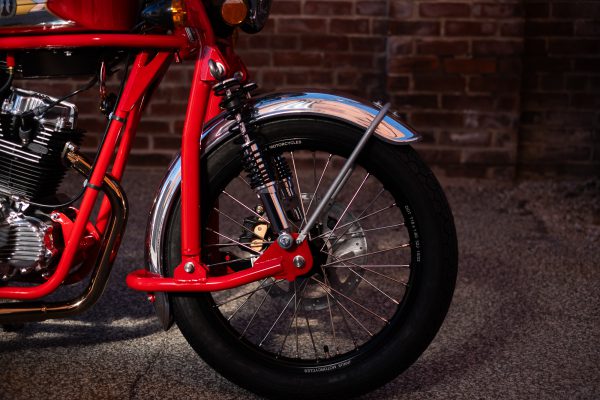 Close-up of red motorcycle's front wheel and suspension with brick wall background.