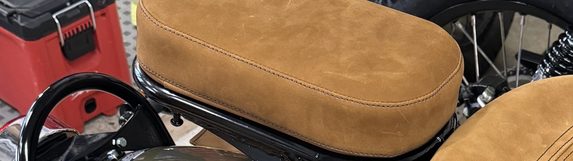 Close-up of brown suede motorcycle seat in a workshop setting.