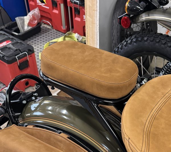 Close-up of brown suede motorcycle seat in a workshop setting.