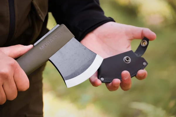 Person holding a Morakniv outdoor axe with a black handle in a forest setting.