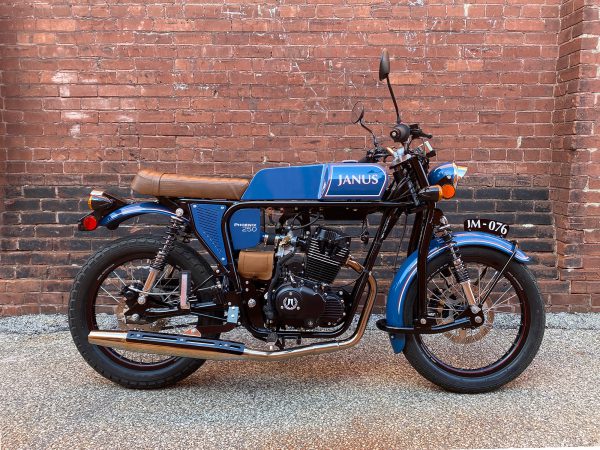 Classic Janus motorcycle parked against a brick wall.