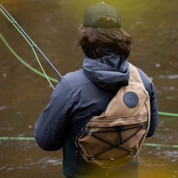 Person fly fishing in a river, viewed from behind, wearing a backpack and cap.